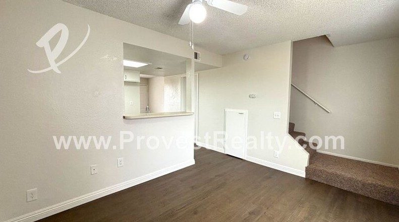 The living room of a two-story townhome, wood-look flooring, the carpeted stairs going up to the bedrooms, and the pass-through to the kitchen.